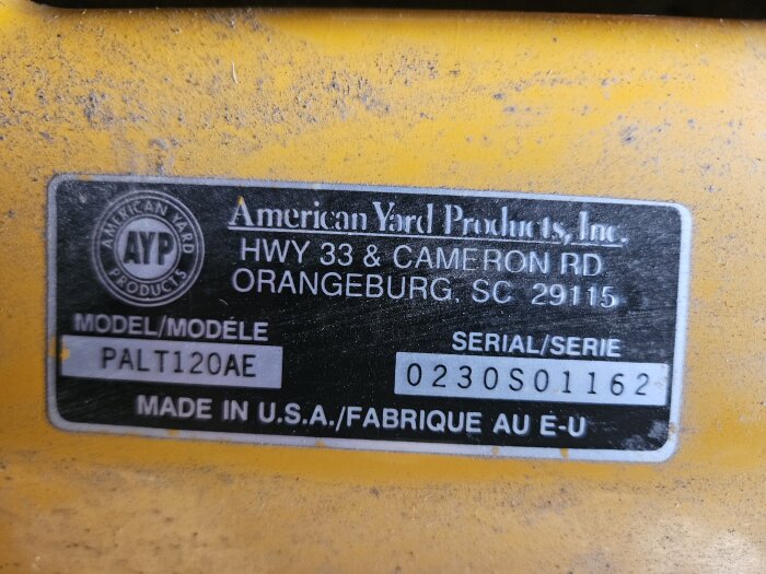 Etikett på åkgräsklippare med texten "American Yard Products" och modellnummer "PALT120AE", samt serienummer "0230S01162".