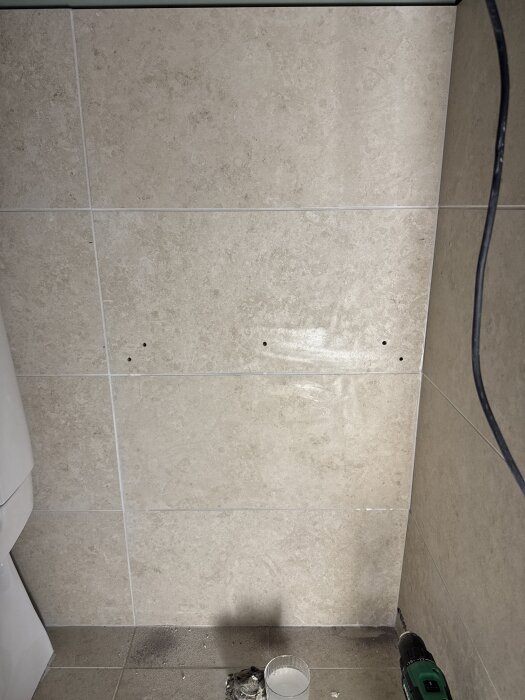 Klinkervägg med borrade hål för montage av en kommod i badrum. En borrmaskin ligger på golvet intill.
