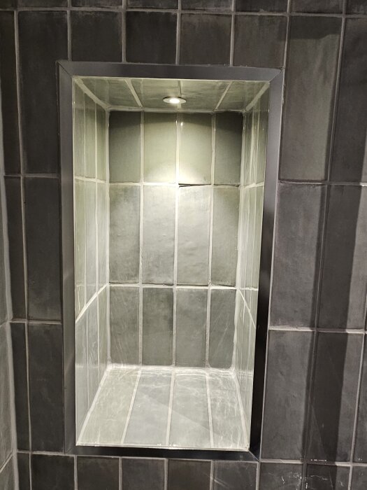 Inbyggd hylla med grön glaserad kakel i ett nyrenoverat badrum.