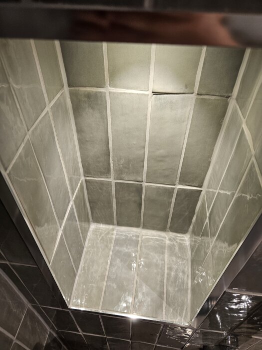 Grönt kaklat hörn i renoverat badrum med belysning ovanifrån.