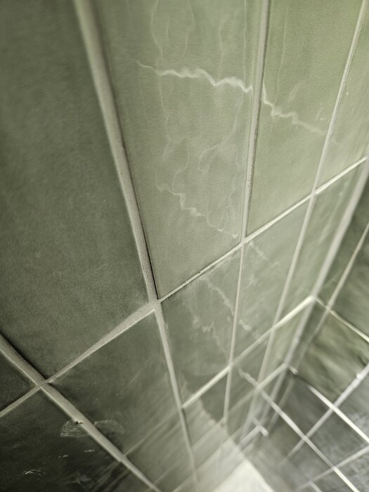 Gröna kakelplattor i ett nyligen renoverat badrum, sett i närbild på väggen.