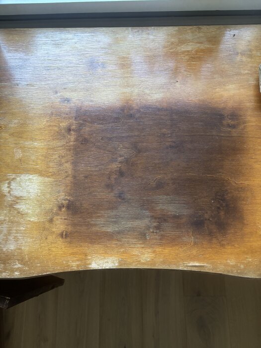 Gammalt skrivbord i faner med mörka fläckar och slitage på ytan, eventuellt från ett skinnunderlägg.