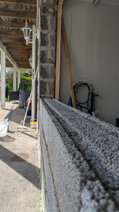 Murade lecablock vid garageöppning under en träveranda, med byggmaterial och verktyg synliga runt omkring.