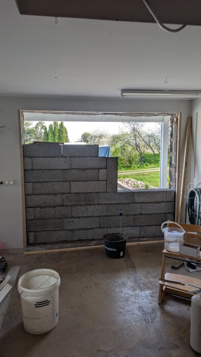 Murad vägg av lecablock under konstruktion i en öppning, med olika byggmaterial runtom, inklusive hinkar och verktyg.