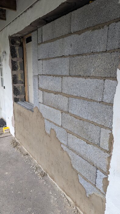 Vägg av lecablock med delvis pålagt puts, under renovering av garagefasad. Grå block med ljusbrun puts på nedre halvan.