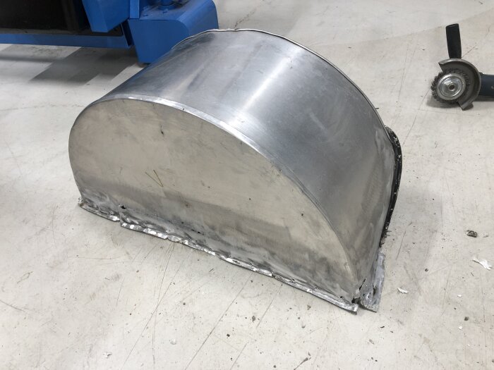 Aluminiumshjulhus bortmonterat från en vagn, placerat på ett golv, med en vinkelslip synlig i bakgrunden.