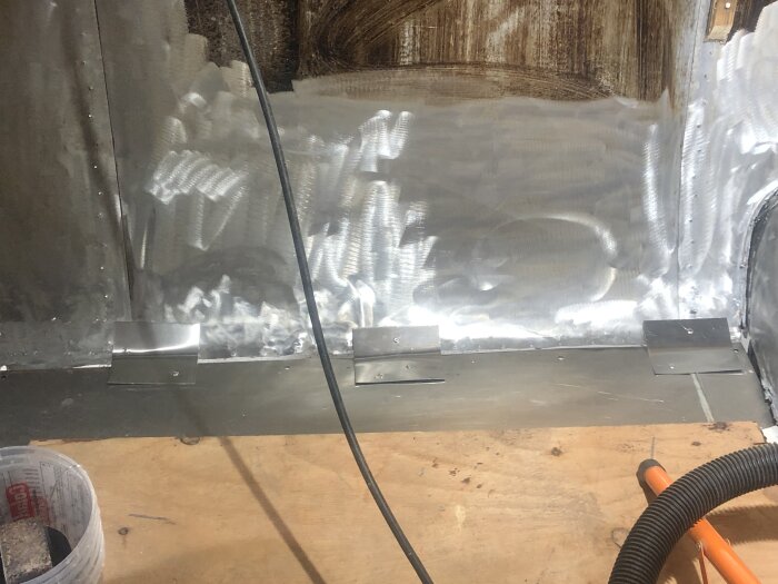 Insida av vagn under renovering, aluminiumplåtar temporärt fastnitade för stöd innan förstärkning med glasfiber; trä, verktyg och kablar synliga.