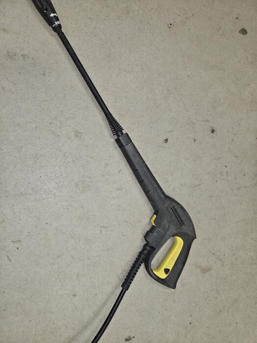Kärcher högtryckstvätt spolhandtag med ansluten slang, liggande på golvet.
