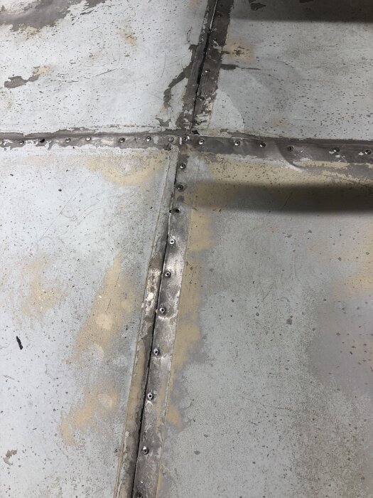 Plåttak med springa och överlappade plåtar som nitats fast, tecken på tidigare vattenläckage. Arbetet visar pågående renovering och tätning.