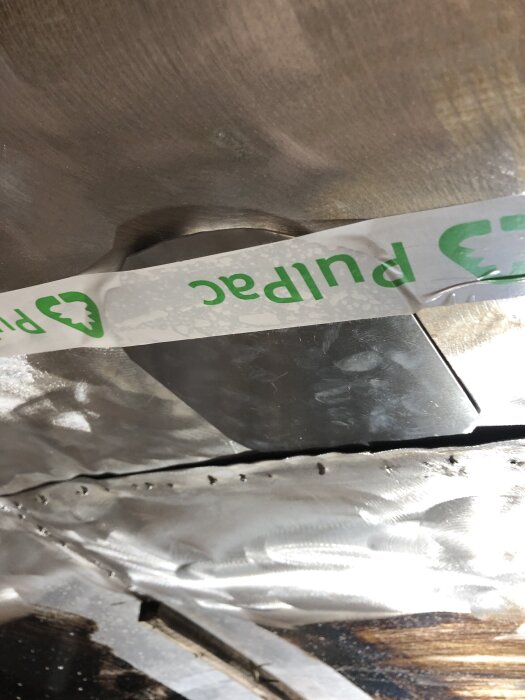 Bild på metallplåt och tejpad skarv i ett tak, del av renoveringsprojekt där hål lagas för att förhindra vattenläckage.