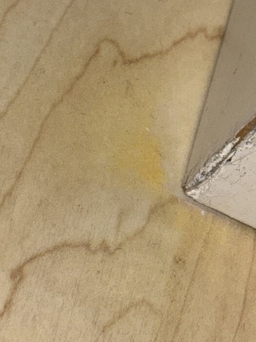 Gulaktiga smulor eller sandliknande material i ett hörn på ett trägolv bredvid en vägg.