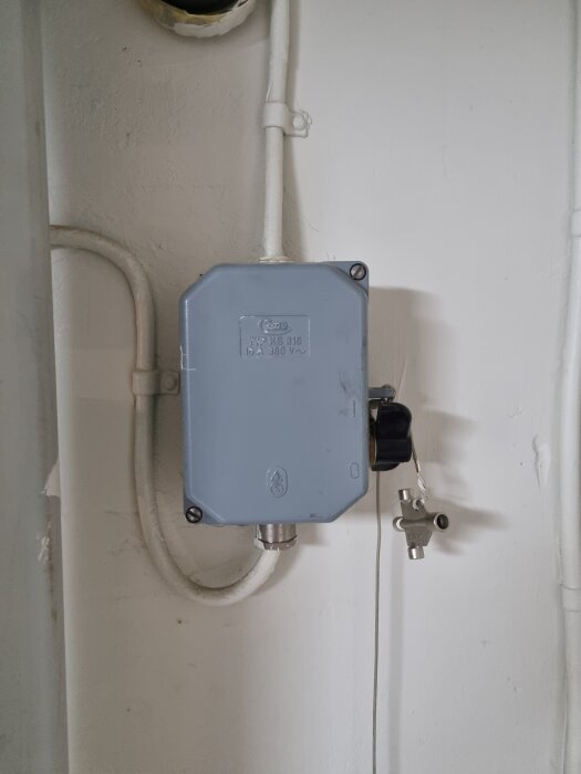 Grå elbox på vit vägg med en nyckel hängande från sidan, diskuterad i ett forum om säkringar och elproblem.