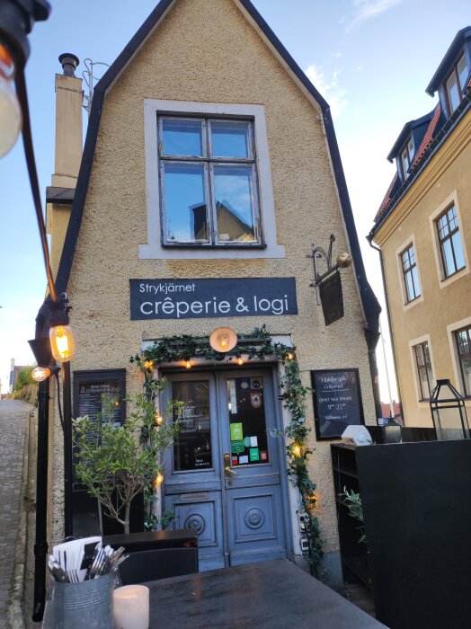 Exteriör av en crêperie och logi med dekorerade dörrar och skylten "Strykjärnet crêperie & logi" i Visby.