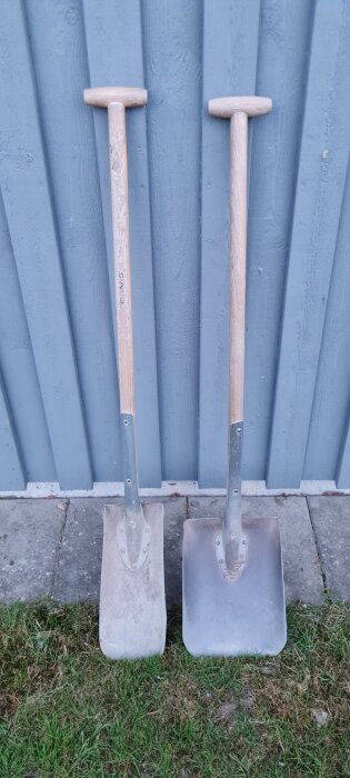 Två Fiskars-skyfflar av modell Classic PRO, lutade mot en blå vägg. Ena skyffeln är mer sliten än den andra.