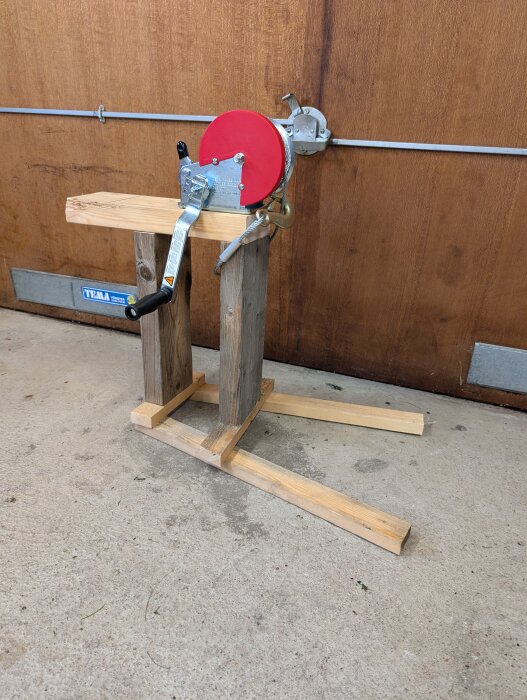 Handvinsch monterad på en träställning med röd navskiva, används för rengöring av skorstenen i ett byggprojekt.