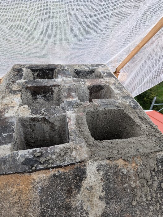 Renoverad tegelmurad skorsten med flera kanaler, omgiven av byggställning och skyddsnät. Nytt bruk är applicerat på murbruket.