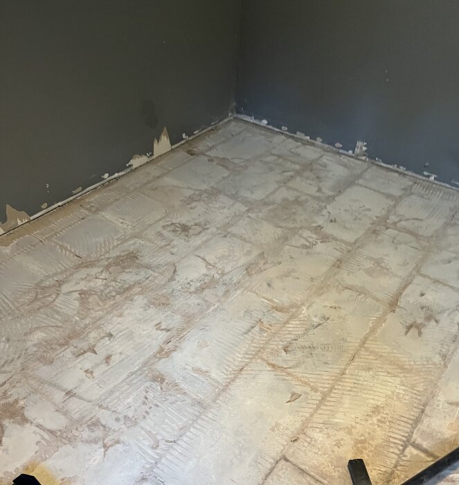 Gammalt, upptaget cementgolv i ett garageförråd med rester av klinker. Väggarnas färg är flagnad, en fråga om ångspärr och golvbeläggning diskuteras.