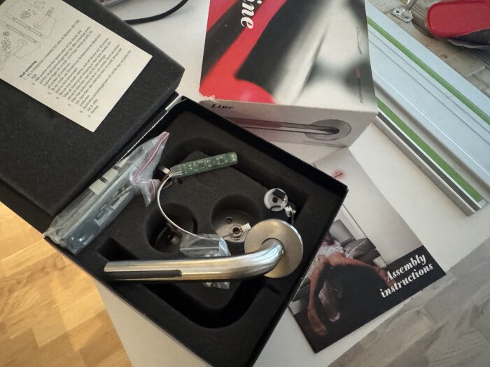 Förpackning med elektroniskt dörrhandtag, komponenter och monteringsinstruktioner.