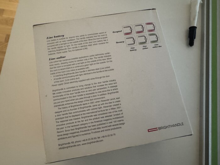 Förpackning av en Brightandle-produkt med text om "line battery" och "line online" funktioner bredvid en penna på ett bord.