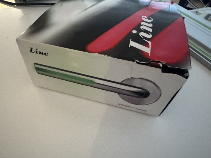 Kartong med texten "Line" och bild på ett dörrhandtag. Förpackningen är lite skadad.