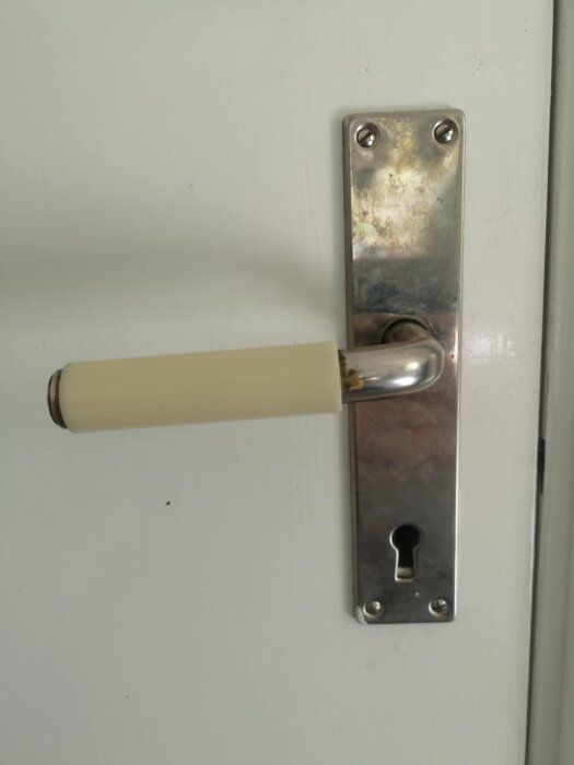 Dörrhandtag i bakelit med nyckelhål på vit dörr, handtaget verkar vara av äldre modell.