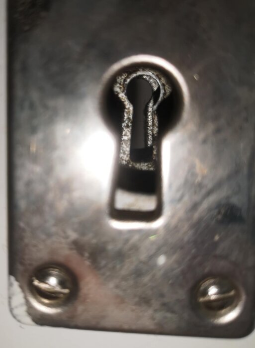 Gammaldags nyckelhål i närbild, omgiven av metallplatta med två skruvar i hörnen.