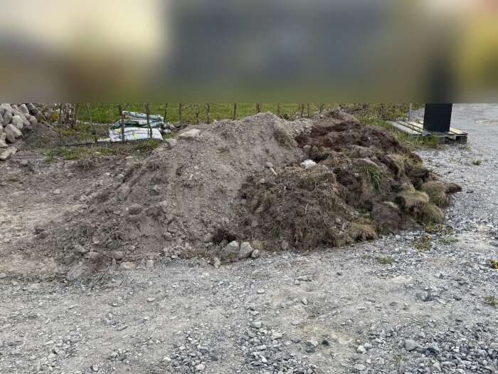 En hög av stenbumlingar och jord/morän, placerad på en grusad yta utomhus, väntar på bortforsling.