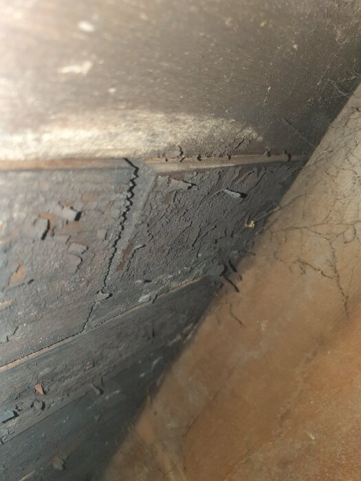 Svart, fjällande yta mellan takstolar, södersidan på vind. Fråga om det är mögel eller behandling. Endast i två bortersta sektionerna.