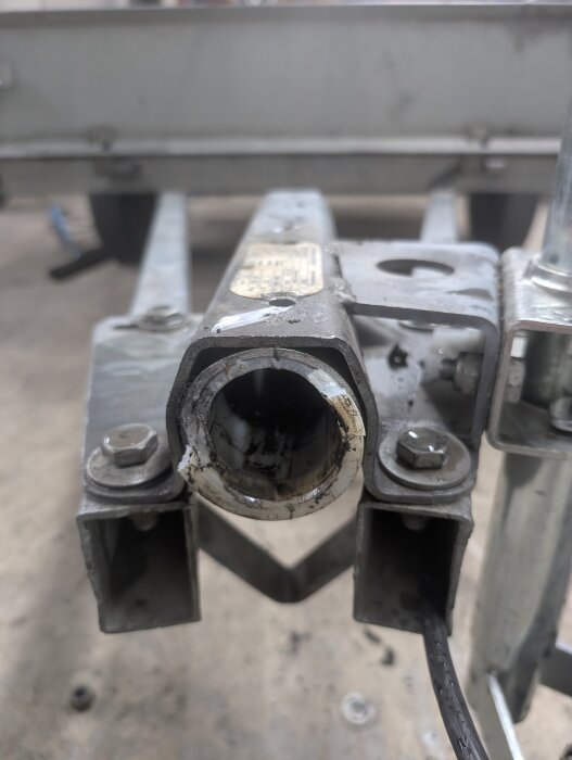 Närbild på ett släpvagnsdrag med borttagna bromsar, där ett rör ska ersätta påskjutsbromsen. Rörets baksida syns med två muttrar.