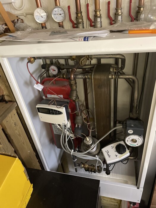 En fjärrvärmecentral med kopparrör, mätare och kontrollpanel installerad i ett hem, eventuellt med läcka i värmeväxlaren.