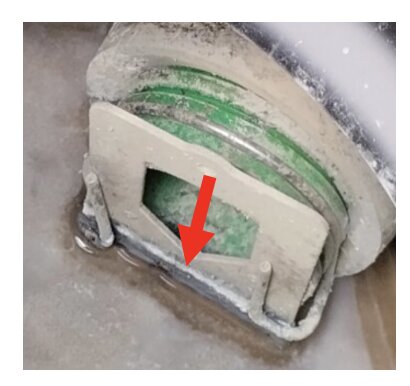 Grå slitsad plastskiva fastkilad under grön komponent, med röd pil pekande på den. Omges av två metallstänger. Behöver justeras med verktyg.