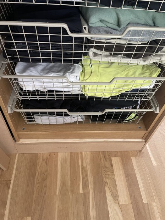Garderobsinredning med PAX-korgar fyllda med vikta kläder, installerade i en träram över ett parkettgolv.