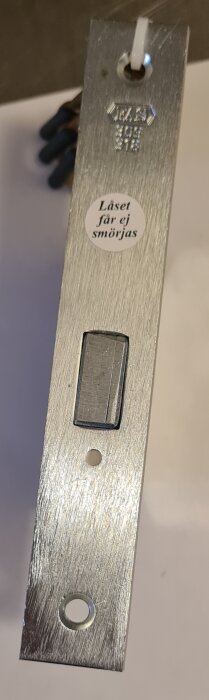 ASSAFAS 309 säkerhetslås i metall med varningsdekal, "Låset får ej smörjas".