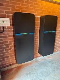 Två väggmonterade svarta batterilagringsenheter med inbyggda växelriktare, installerade på en tegelvägg i ett garage eller teknikutrymme.
