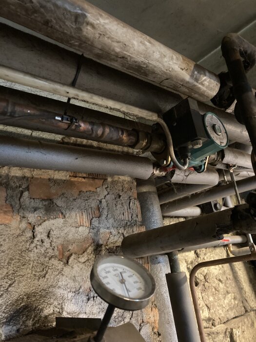 Rörsystem med temperatur- eller tryckgivare monterad efter pumpen, inomhusmiljö med synligt murverk.