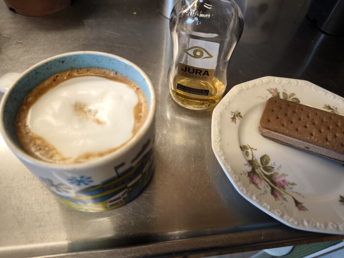 Cappuccino i mugg, Jura whiskyflaska och chokladglass-sandwich på tallrik.
