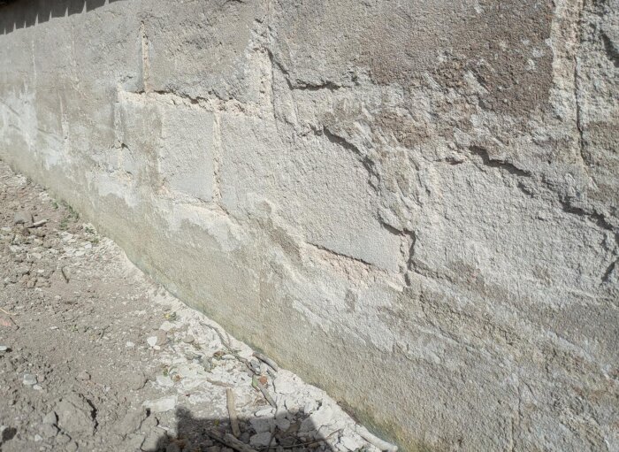 Betongsockel med slätslipade och skadade ytor. Kratrar och missfärgningar syns, troligen salt/kalkavlagringar. Byggprojekt från tidigt 80-tal.