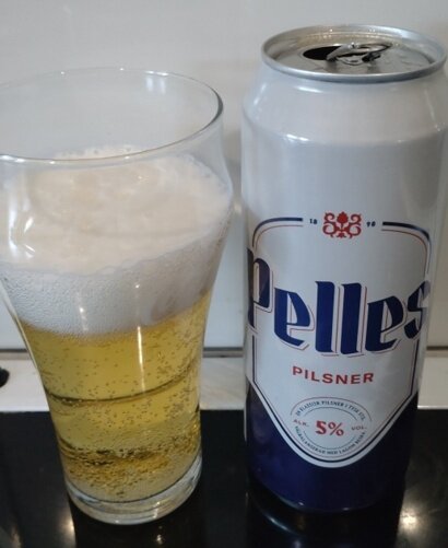 En ölburk med texten "Pelles Pilsner" bredvid ett glas med öl och skum på toppen.