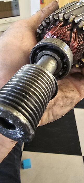 Närbild av en hand som håller en elmotorarmatur med exponerade kopparlindningar och synliga lager i lagerhus.