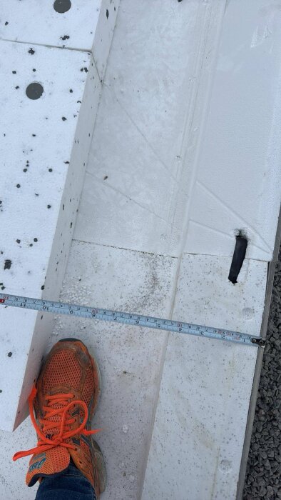 Mansfot med orange sko bredvid en vit Sundolit kantavslutning. En måttstock mäter avståndet.