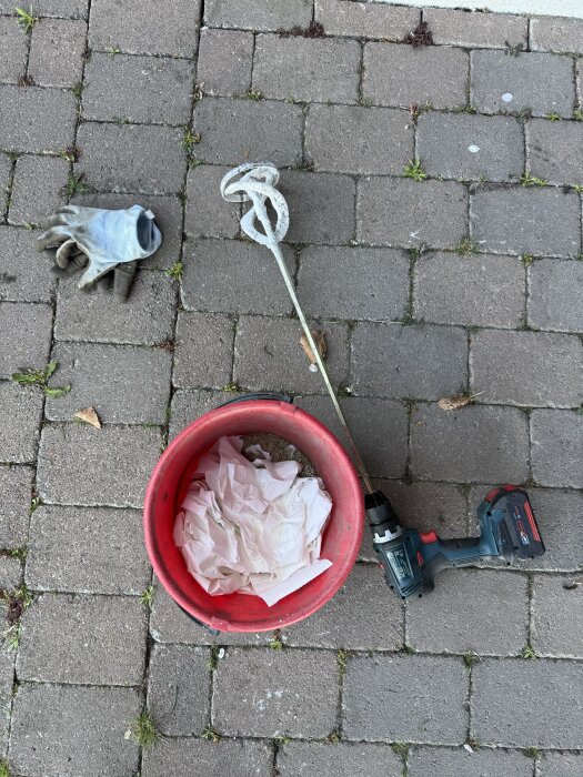 Röd hink med toapapper, borrmaskin med mixerfäste och arbetshandske på stenbelagd yta. Används för gräsmix enligt forumtips.