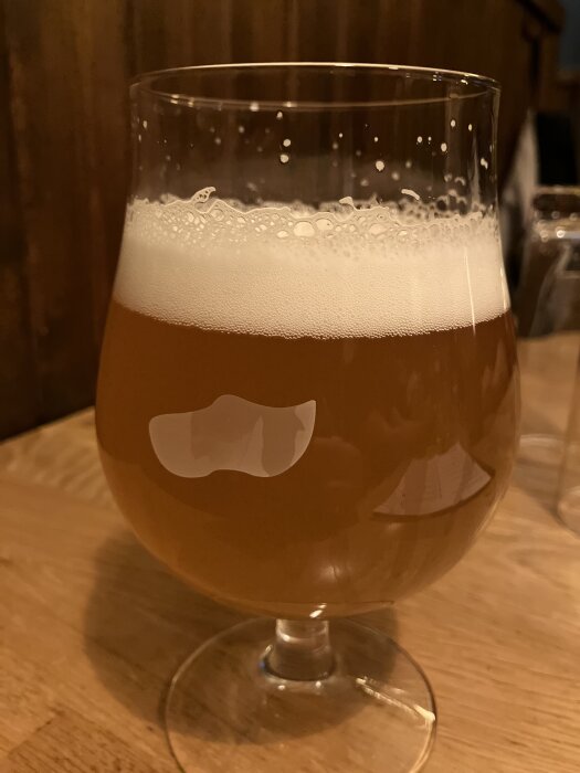 Ett glas fyllt med skummande öl på ett träbord.