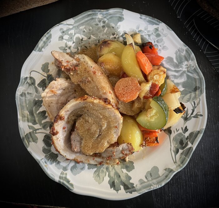 Tallrik med porchetta och ugnsstekta grönsaker som potatis, morot, palsternacka, squash, lök och paprika på ett blommigt fat.