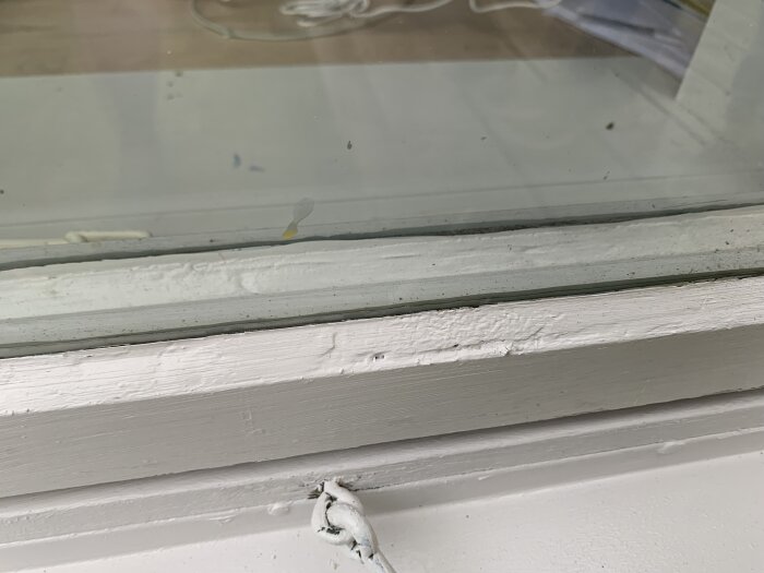 Närbild av ett nymålat fönster med ojämn yta och skador, troligen orsakat av målning i dåligt väder. Viss avflagning syns på färgen.