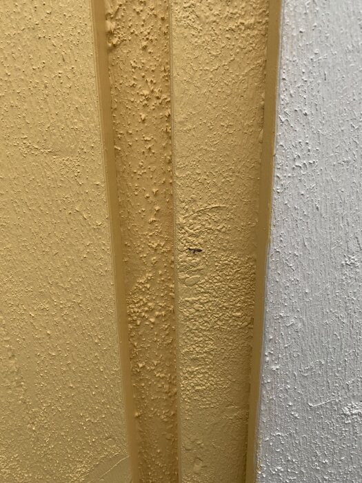 Närbild av en ojämnt målad fasad med gul färg; texturen är knottrig och väggytan ser oslipad ut.