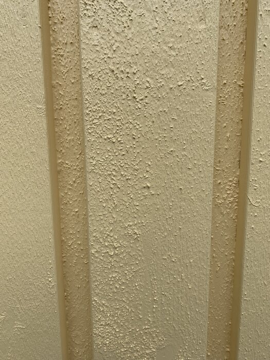 Nymålad fasad med ojämn struktur, blåsor och skrovlighet synliga på ytan efter regn, vilket visar på bristfälligt utfört måleriarbete.