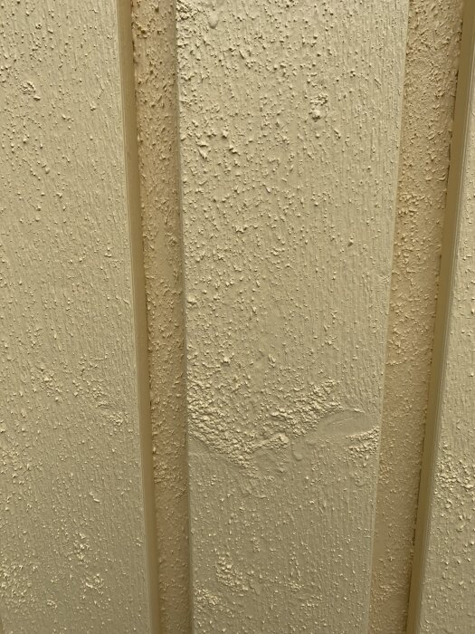 Gulmålad träfasad med ojämnt och bubbligt färglager, möjligen påverkad av regn vid målning.