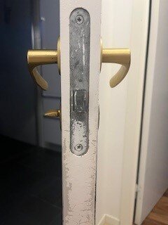 Gammalt låshus på dörr med mässingshandtag, utan synlig nummerbeteckning, som behöver ersättas.