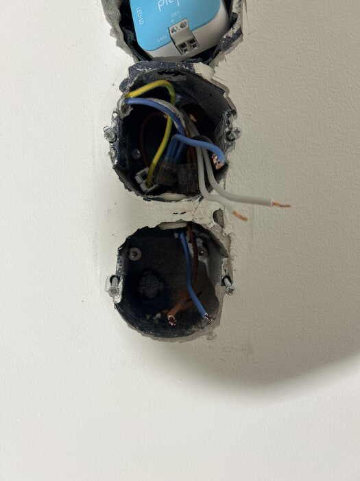 Elektriska dosor i tegelvägg med synliga sladdar, den övre dosan installerad skevt och omgiven av puts.