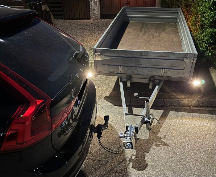 Bil och släp parkerade, med anslutet elkablar; släpvagnens belysning är på.